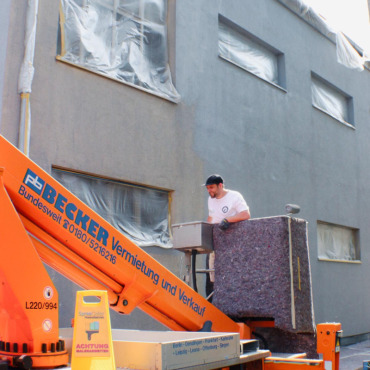Mitarbeiter führt Malerarbeiten an der Fassade mit Hubarbeitsbühne aus
