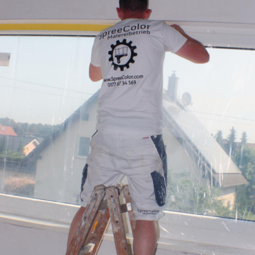 Mitarbeiter der SpreeColor Malereibetrieb GmbH bei Malerarbeiten an einem Fenster im Neubau